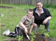 Mother and son sat on the grass planting tomatoes